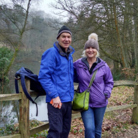 A man and woman in full walking gear by a stream in a forest.