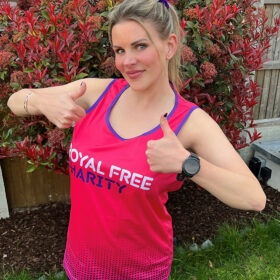 Woman standing in a garden wearing a Royal Free Charity running vest, smiling at the camera with her thumbs up.