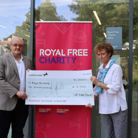 Two people stood outside the Royal Free Charity office with a banner between them, holding up a large display cheque for £10,000.
