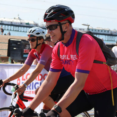 Two cyclists in Royal Free Charity branded sports vests, riding their bikes by Brighton Pier.