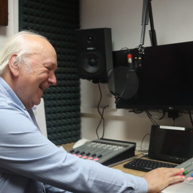 Man sat in front of a mic at a radio desk smiling.