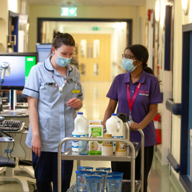 Volunteer pushing a tea trolley with an NHS member of staff.