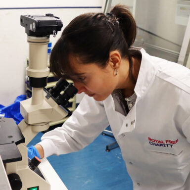 Woman in lab coat looking through microscope in laboratory.