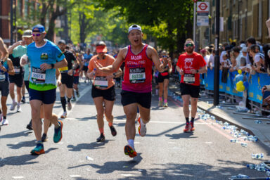 A man wearing a Royal Free Charity running vest, running with other participants on a busy London road.