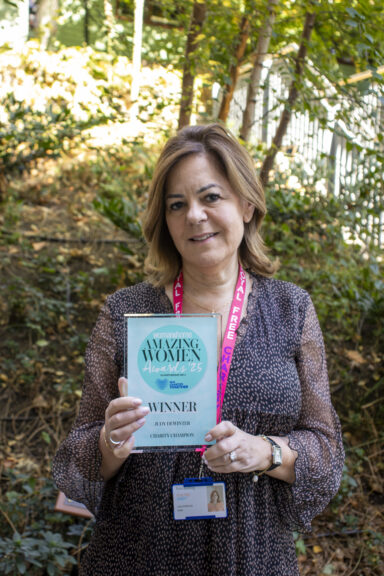 A woman standing in front of green trees holding an Amazing Women Award.