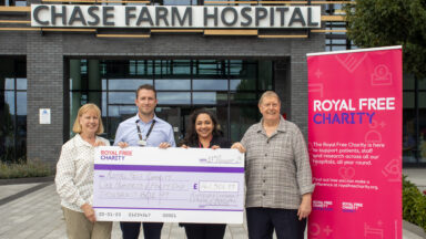 Two men and two women holding a big cheque for £141,501.99, standing in front of Chase Farm Hospital.