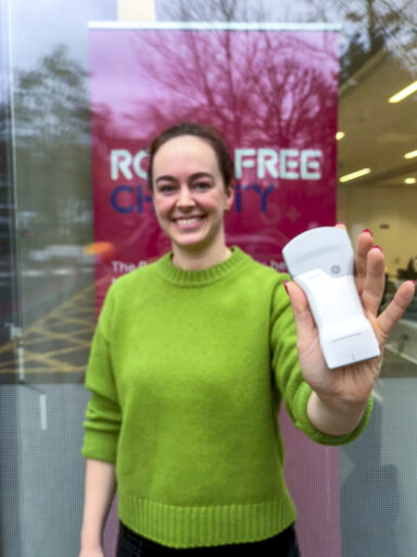 A woman in a green jumper is holding a pocket-sized ultrasound scanner towards the camera.