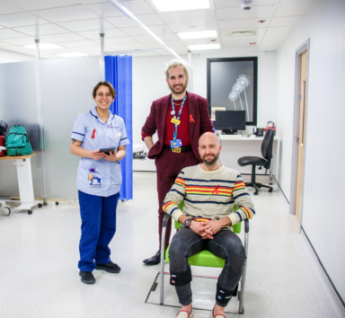 A man and woman (in scrubs) standing beside a person in a wheelchair in a hospital ward.