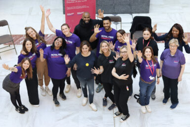 A group of staff wearing Royal Free Charity t-shirts, with their hands up in the air, smiling.