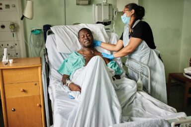 Man lying in hospital bed receiving a massage from a complementary massage therapist.