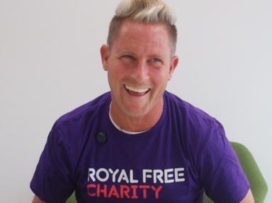 Man laughing. He is wearing a purple t-shirt that says Royal Free Charity