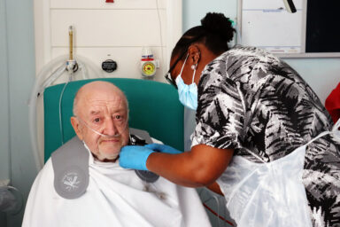 Woman shaving a male patient's face in hospital.