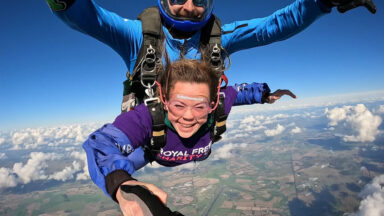 A woman wearing a Royal Free Charity t-shirt, skydiving high above with a professional instructor on her back.
