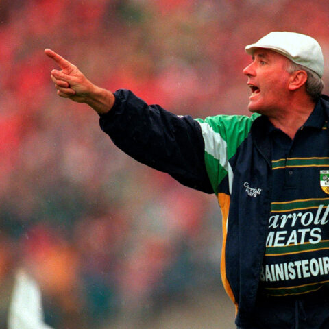An animated sports coach wearing a white cap and a Carroll Meats-branded jacket passionately gestures on the sidelines during a game, pointing in the direction of the action.