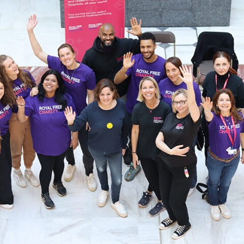A group of people engaged in face-to-face fundraising at the Royal Free Charity, indoors with a fundraising banner and materials, interacting warmly with members of the public.