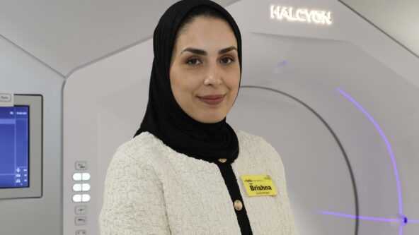 A radiographer standing in front of a white radiotherapy machine.
