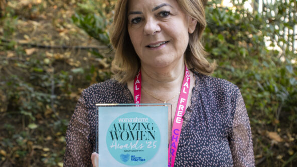 A woman standing in front of green trees holding an Amazing Women Award.