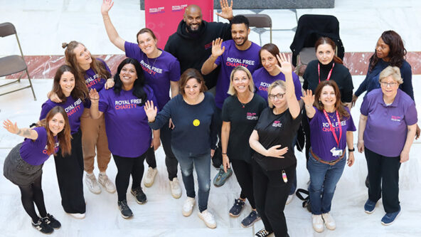 A group of people engaged in face-to-face fundraising at the Royal Free Charity, indoors with a fundraising banner and materials, interacting warmly with members of the public.