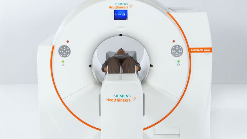 A Siemens Healthineers PET scanner in a medical imaging room, showing the machine's large gantry with patient bed and control panel, used for advanced diagnostic imaging.