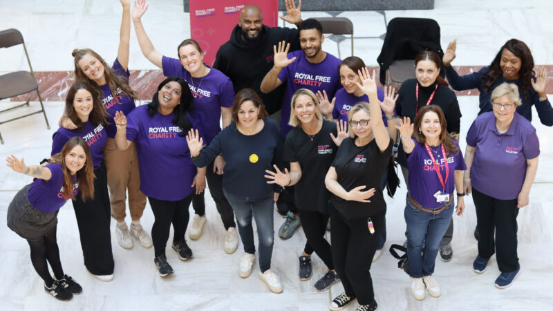 A group of staff wearing Royal Free Charity t-shirts, with their hands up in the air, smiling.