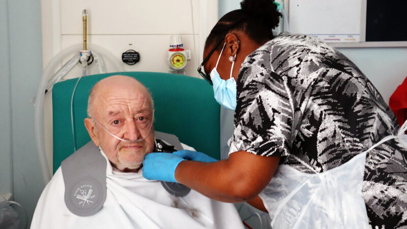 Woman shaving a male patient's face in hospital.