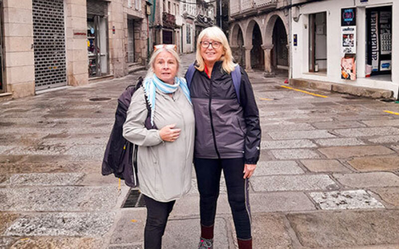 Two women standing in raincoats in a rainy cobbled street.