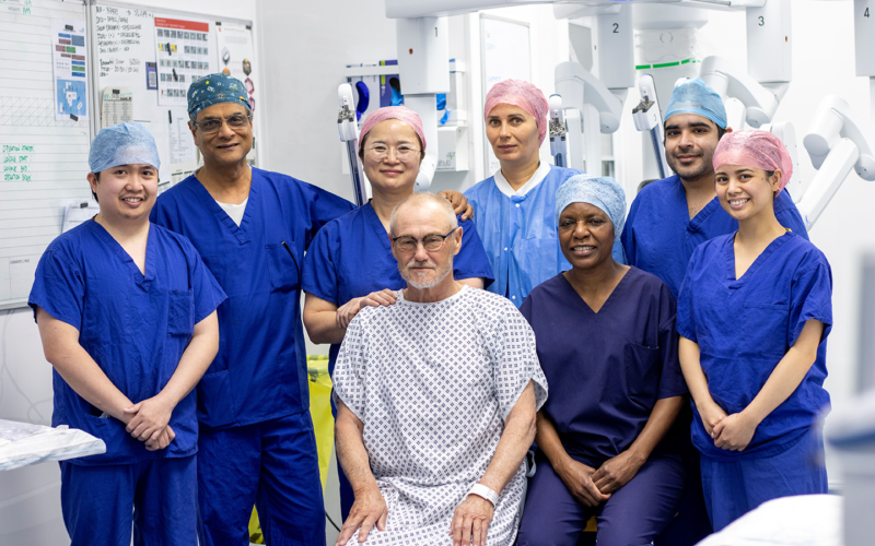 A group of doctors in scrubs, surrounding a patient in a gown, all in front of the new surgical robot.