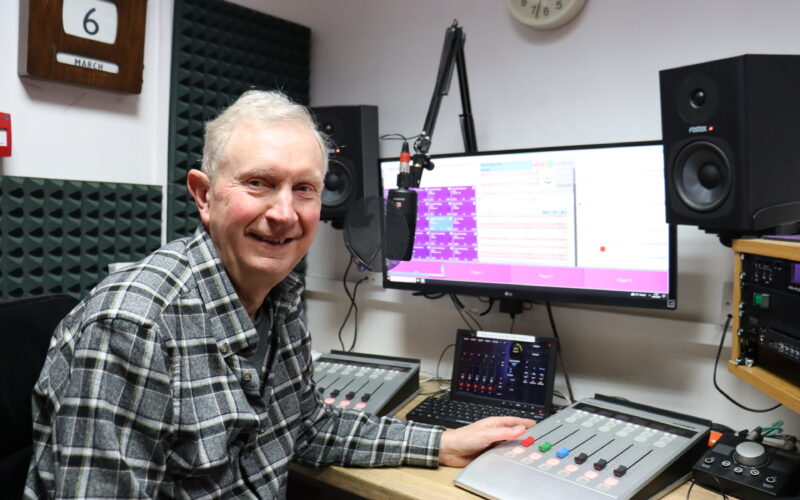 Man sat at a radio desk, smiling at the camera.