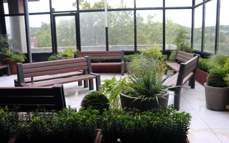 A rooftop garden with brown benches and green plants.