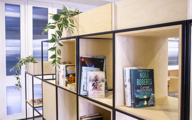 A beige bookshelf with books of varying sizes and a green plant.