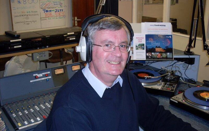 A man wearing radio headphones sat at a radio desk while smiling at the camera.