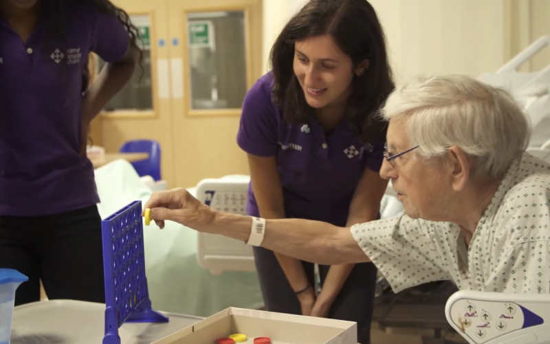 Volunteer at a patient's bedside talking to them,