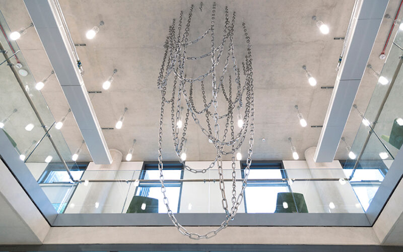 A sculpture made of metal links, like a series of connected chains. It hangs suspended from the ceiling.