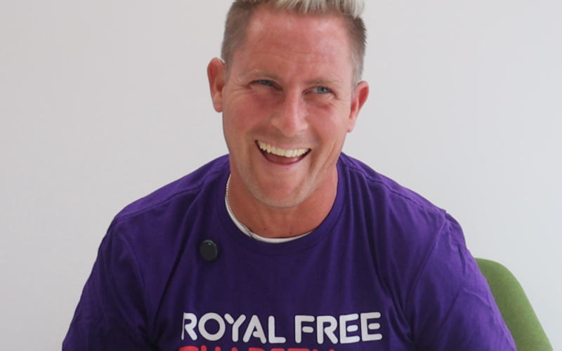 Man laughing. He is wearing a purple t-shirt that says Royal Free Charity