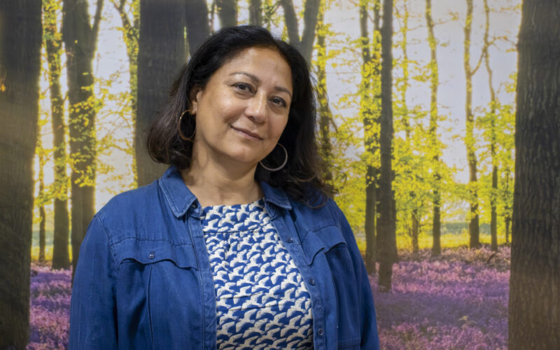 A headshot of a woman standing against a wall featuring tree wallpaper.