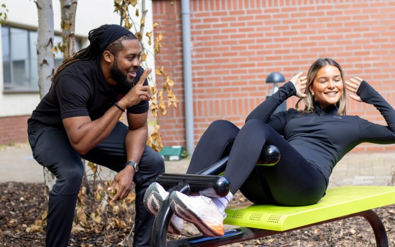 Man kneeling beside a woman on an exercise bench doing a crunch.