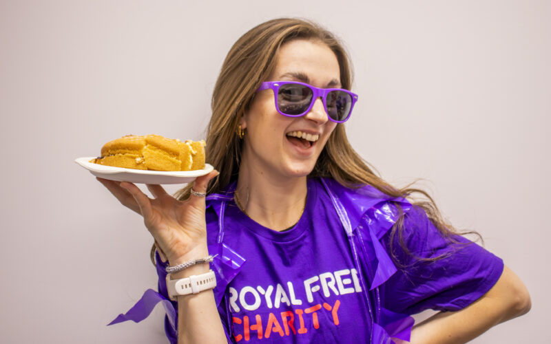 A supporter wearing a Royal Free Charity T-shirt and purple glasses holds a slice of cake during a tea party fundraiser.