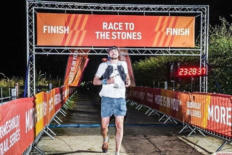 Man in full running gear crossing the finishing ine of the Race to the Stones 100km ultramarathon.