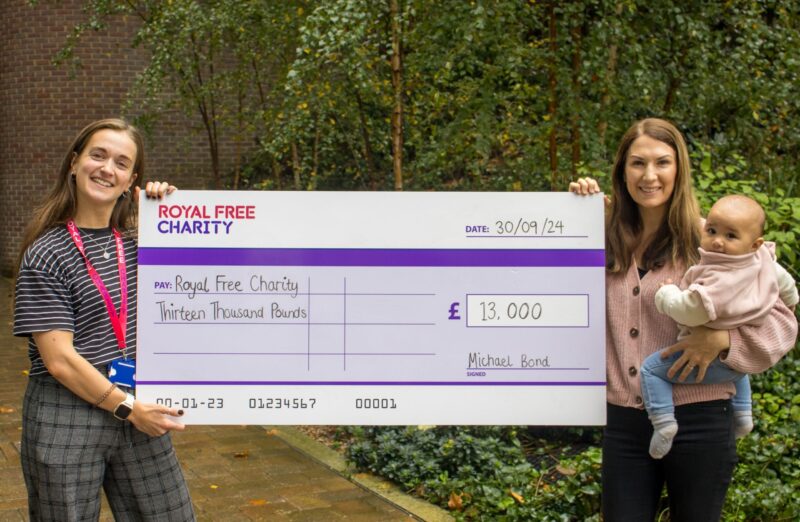 Two women, one with a baby, holding a large display cheque with £13,000 written out to the Royal Free Charity.