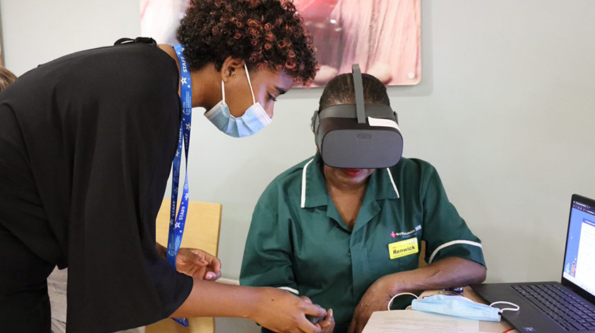 Woman in mask leaning over nurse wearing VR headset