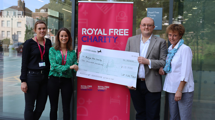 Four people outside the charity office holding a large model cheque for £10,000