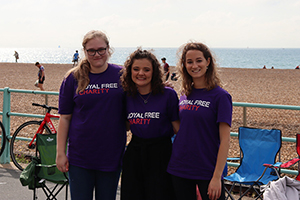 Three women in branded Royal Free Charity t-shirts cheering on cyclists at the London to Brighton cycle race, 2022