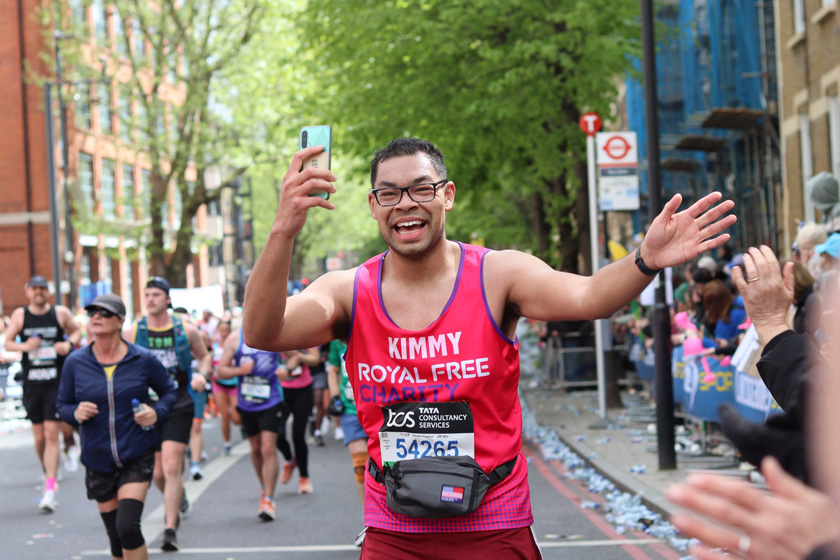 Man in Royal Free Charity running gear holding a phone running on the street with other runners.