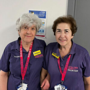 Close up of two women stood together in a corridor both wearing Royal Free Charity volunteer t-shirts. 