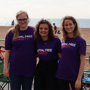 Three people in Royal Free Charity t-shirts stood in front of beach. 